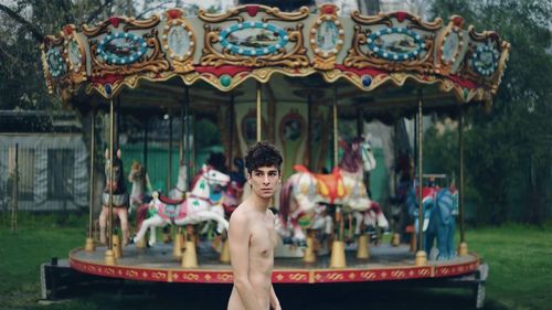 Side view of shirtless young man standing at amusement park