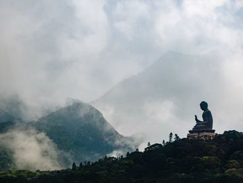 Buddha statue against mountains and cloudy sky