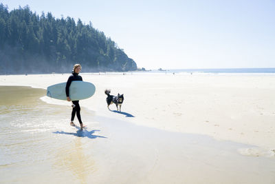 Portrait of happy man holding surfboard with dog walking at beach