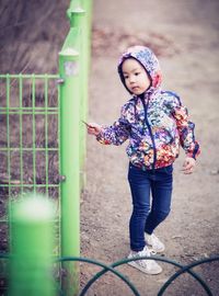 Girl wearing hooded sweatshirt walking by green metallic fence