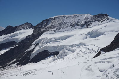 Low angle view of snowcapped mountains against clear blue sky