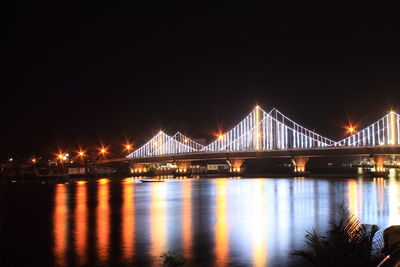 Illuminated bridge over river against sky at night