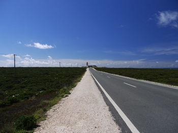 Empty road amidst field against sky