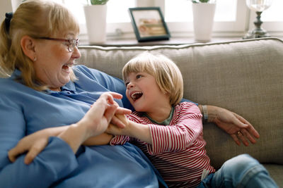 Playful boy with grandmother on sofa in living room at home