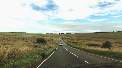 Empty road amidst field against sky