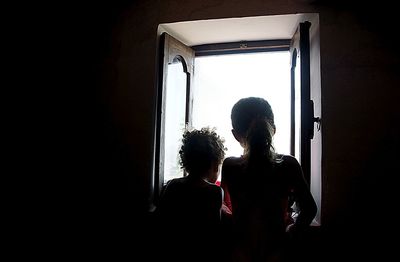 Rear view of boys looking through window at home