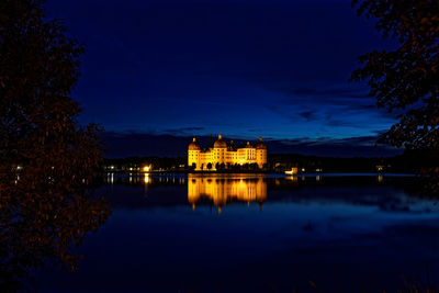 Illuminated buildings by lake against sky at night