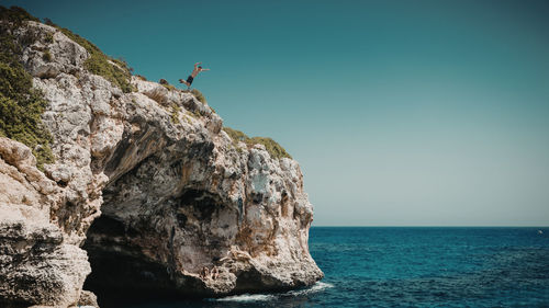 Low angle view of man jumping from cliff against sky