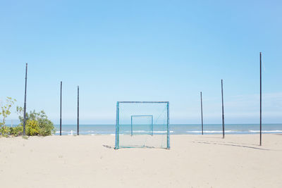 Soccer goal on sand against clear sky at beach