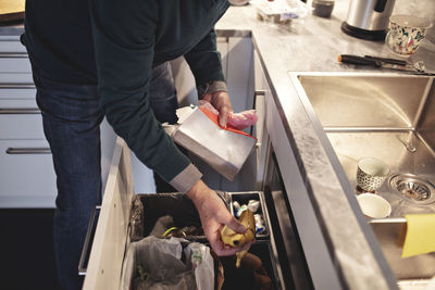 Midsection of senior man throwing garbage in dustbin at home