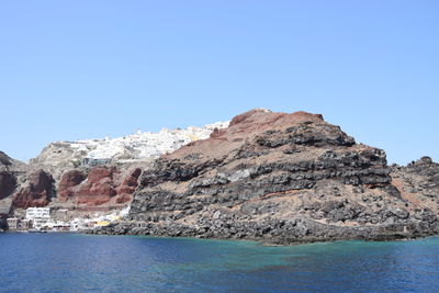 Rock formations by sea against clear blue sky