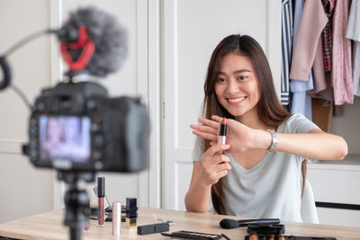 Smiling woman blogging while holding lipstick on table