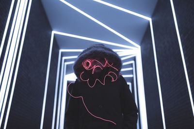 Woman in hooded clothing with light painting standing against illuminated lights