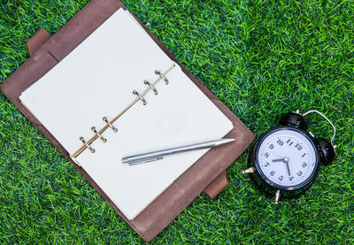 High angle view of diary and pen by alarm clock on grass