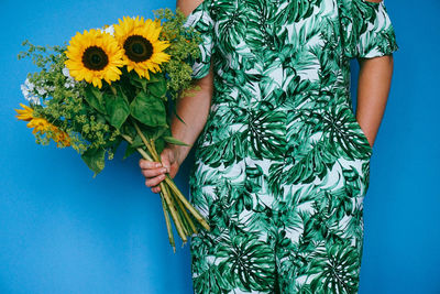 Close-up of hand holding yellow flower against blue background