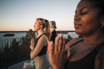 Woman with hands clasped exercising with female friends at patio