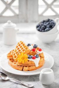 Waffles with blueberries, red currants, poured with yogurt on a white plate on the windowsill