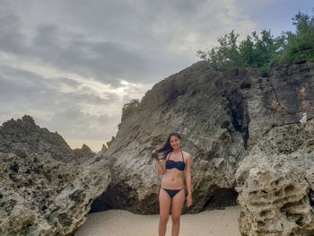 Young woman standing on rock against sky