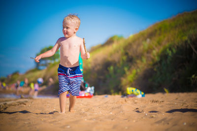 Full length of shirtless boy on sand at beach