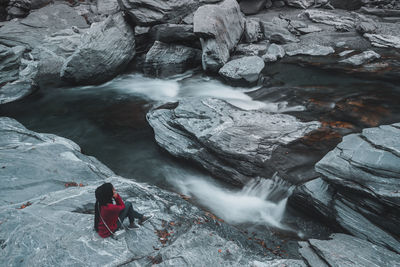 Woman sitting on rock by stream in forest