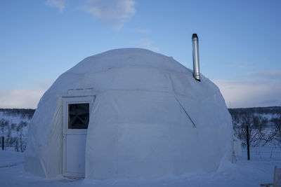 Snow covered field by building against sky