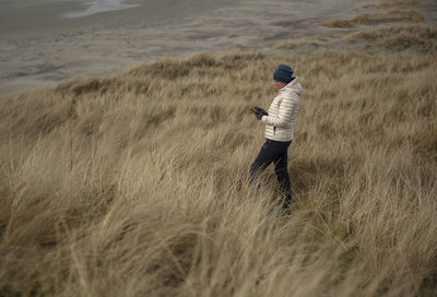 Full length of woman using mobile while standing amidst grass