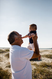 Grandfather holding grandson while standing on beach