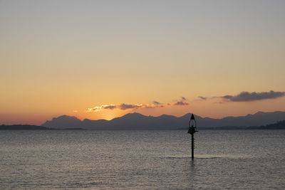 Silhouette person standing by sea against sky during sunset