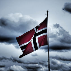 Low angle view of norwegian flag against cloudy sky