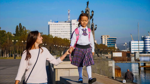 Full length of friends on woman in city against sky