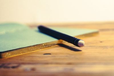 Close-up of pencil with book on wooden table