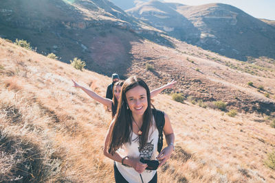 Portrait of smiling young woman with arms raised on mountain