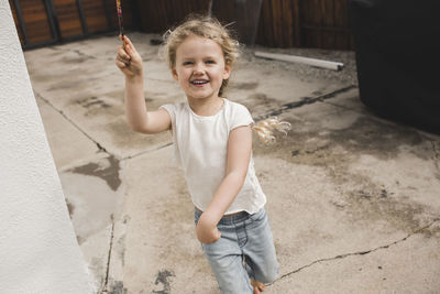 Portrait of happy girl playing with magic wand outside house