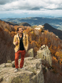 Traveler is standing on high rock, enjoying the view and looking up. hiking in autumn time.