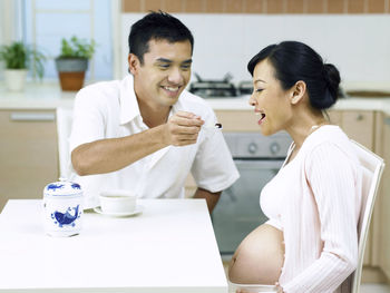 Man feeding pregnant wife while sitting at table in home