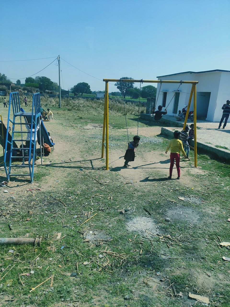 nature, grass, men, sky, group of people, day, playground, lifestyles, childhood, leisure activity, plant, outdoors, sports, land, architecture, built structure, child, clear sky, sunlight, full length, women, adult, outdoor play equipment, field