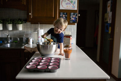 Happy toddler girl sitting on counter helping bake muffins