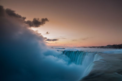 Scenic view of waterfall against sky at sunrise