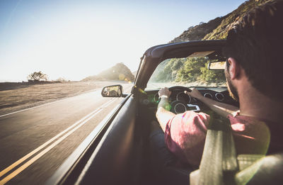 Rear view of man driving car against sky