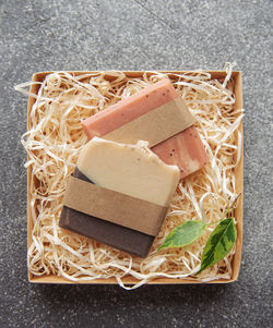Assorted natural handmade soap bars and green leaves in box on a straw background