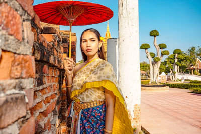 Young woman holding umbrella standing against wall