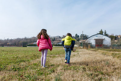 Rear view of three children walking home with small child riding piggyback