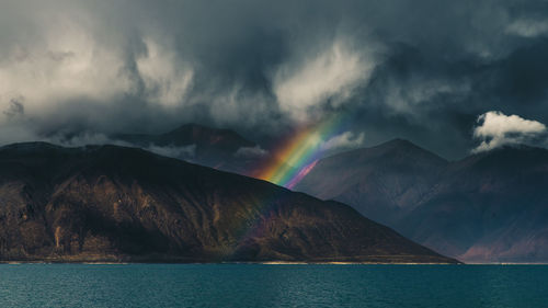 Rainbow over lake and mountains against sky