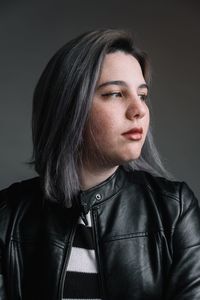 Close-up of thoughtful teenage girl wearing leather jacket against gray background