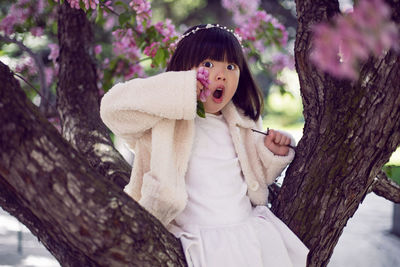 Korean girl in a white light fur coat and a headband sitting on a tree branch in a garden