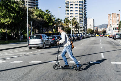 Mature man commuiting in the city with his kick scooter, crossing a street