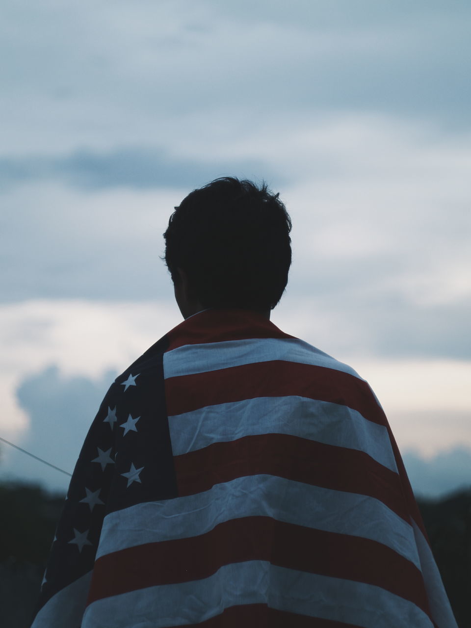 REAR VIEW OF BOY STANDING AGAINST CLOUDY SKY