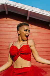 Trendy african american female with red lips and short hair dancing while shouting against house wall