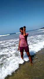 Cheerful woman looking away standing at beach against sky