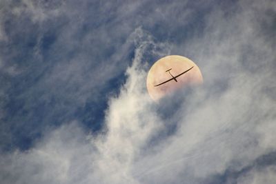 Low angle view airplane flying in sky against full moon 